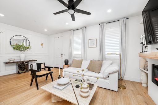 Modern living room with stylish decor, white sofa, and wooden accents, featuring a ceiling fan and natural light.