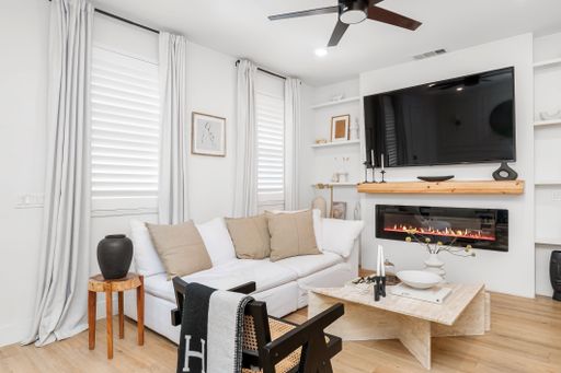 Modern living room with white sofa, fireplace, and large TV, featuring neutral decor and wooden accents, creating a cozy atmosphere.