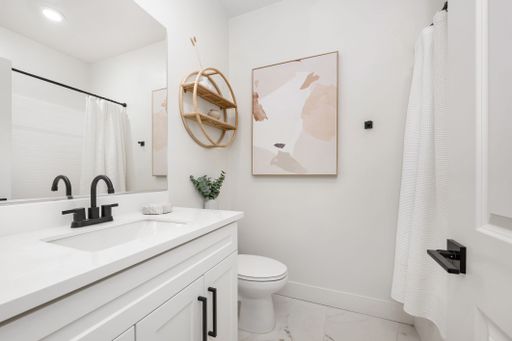 Modern white bathroom interior with black fixtures, abstract art, and minimalist decor.