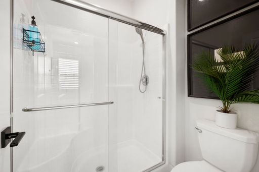 Modern bathroom with glass shower enclosure and potted plant, featuring bright white tiles and sleek fixtures.