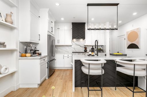 Modern kitchen interior with white cabinets, marble countertops, and stylish lighting, featuring a sleek design and wooden flooring.