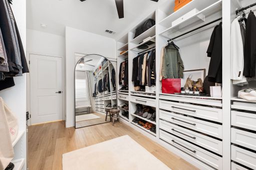 Spacious modern walk-in closet with organized clothing, shoes, and accessories, featuring a large mirror and bright lighting.