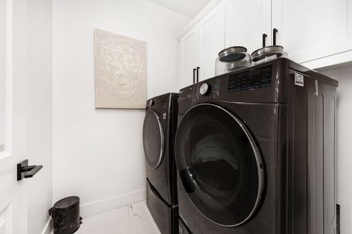 Modern laundry room with sleek black washer and dryer set, white cabinetry, and minimalist decor.