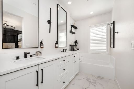 Modern bathroom with white cabinets, black fixtures, and a bathtub under a window with shutters.