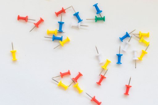 A pile of colorful push pins on a plain white background, ideal for office or school themes.