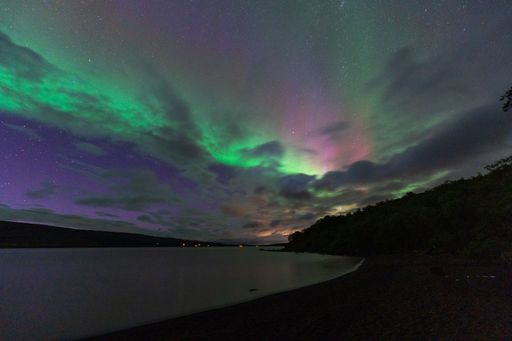 Stunning Northern Lights over a tranquil lake with vibrant green and purple hues illuminating the night sky.