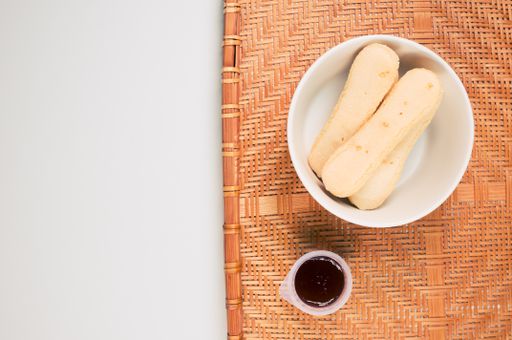 A high angle shot of a bowl of cookies and jam on a woven fabric on a white surface