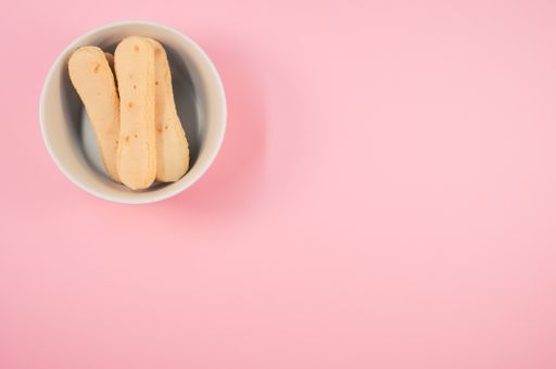 A high angle shot of a bowl of cookies on a pink surface