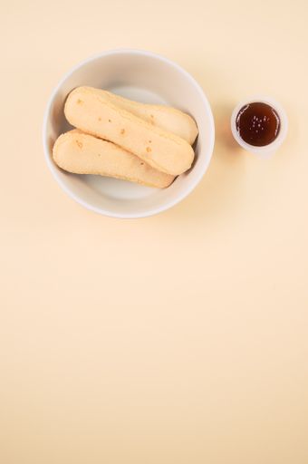 A vertical shot of a bowl of cookies and jam on an orange surface