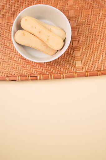 A vertical shot of a bowl of cookies on a woven fabric on an orange surface
