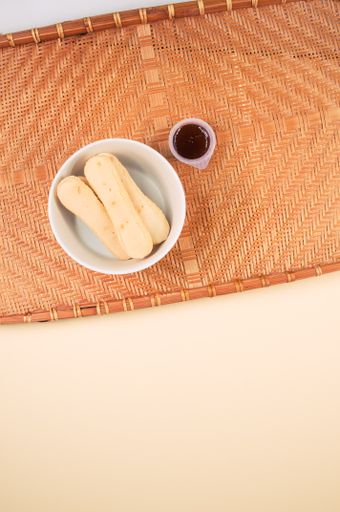 A vertic shot of a bowl of cookies and jam on a woven fabric on an orange surface
