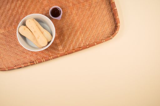A top view of ladyfinger cookies with ketchup dip on a bamboo wicker tray isolated on pink background