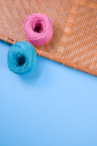 A vertical shot of blue and pink yarn on bamboo wicker tray isolated on blue background