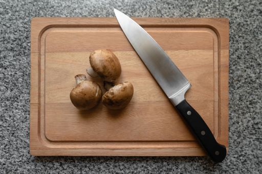 A top view of the three champignon mushrooms on the wooden cutting board with a sharp knif