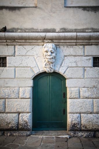 A small door with a decorative mask over it in Venice, Italy
