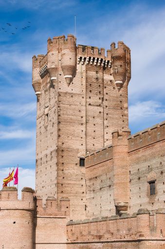 A vertical shot of La Mota Medina castle tower with flags in the daylight