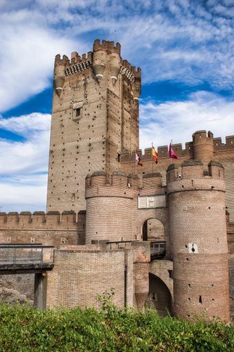 A vertical shot of La Mota Medina castle and tower with flags in the daylight