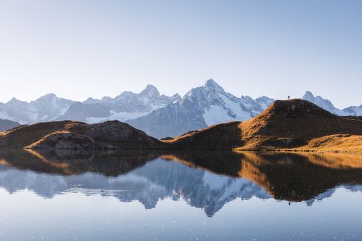 Autumn landscape view of a mountain range reflecting in a lake with a silhouette standing on an illuminated hill at golden hour