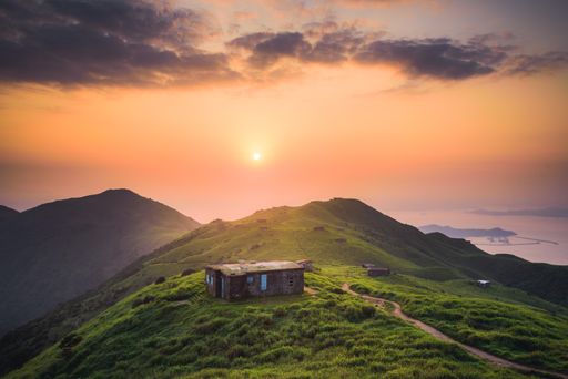 A beautiful shot of a small house built on a peaceful green hill high up in the mountains