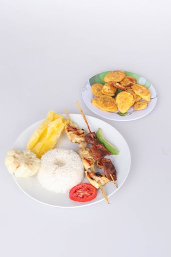 A closeup of the grilled meat on the skewer with rice and veggies on a plate