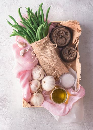 A top view of a vegetable box with garlic, oil, and green beans