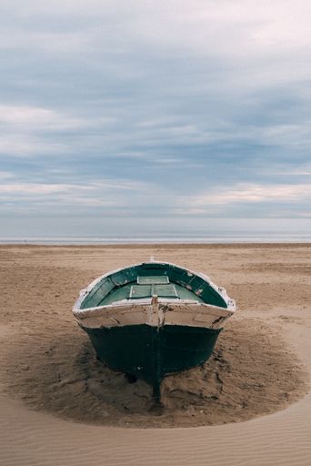 A vertical shot of a green wooden boat on a sand seashore
