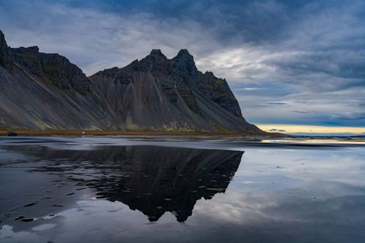 Stunning reflection of Vestrahorn mountain on a calm water surface under a dramatic cloudy sky in Iceland.