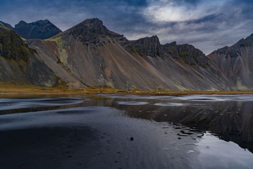 Stunning view of Vestrahorn mountain reflecting in the calm waters of a black sand beach in Iceland under a dramatic sky.