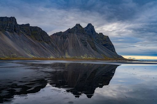 Stunning view of Vestrahorn mountain reflected in the calm waters of Stokksnes beach, Iceland, under a dramatic cloudy sky.