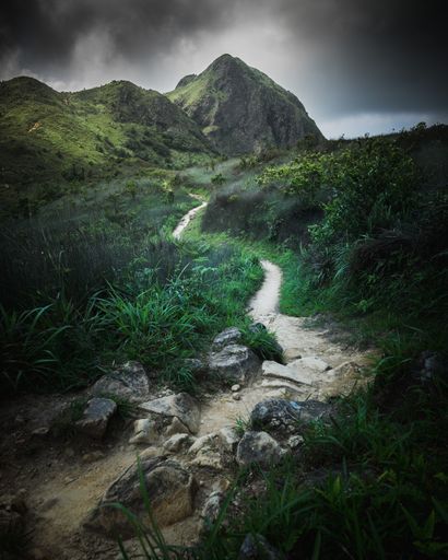 A beautiful shot of a steep slopy road of a hill leading to a rocky mountain with dark clouds around