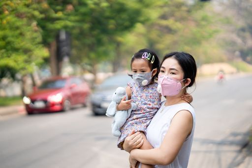 A young Thai mother holding her little daughter in her arms both wearing protective face masks