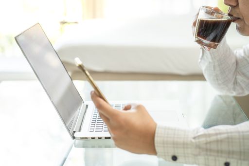 A businessman working through his laptop and mobile phone while drinking coffee - work from home concept