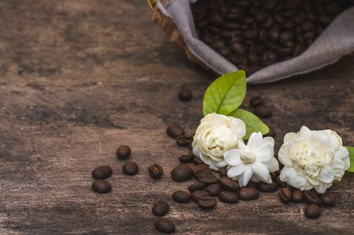 A closeup shot of coffee beans and jasmines on a wooden surface