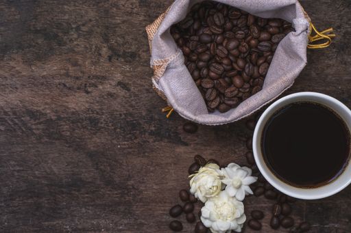 A top view of cup of coffee, beans, and jasmines on a wooden surface