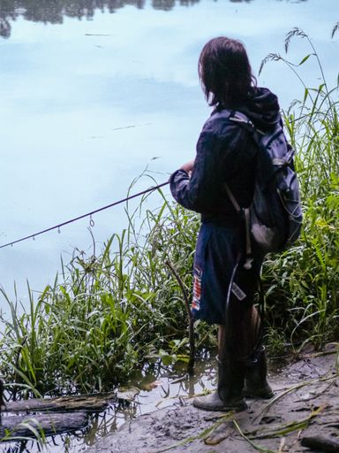 A vertical shot of a Caucasian fisherman catching fish with a rod standing on a bay
