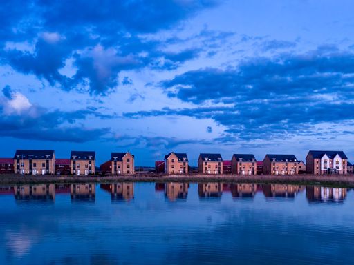 Row of modern houses reflected in a calm lake under a vibrant blue evening sky.