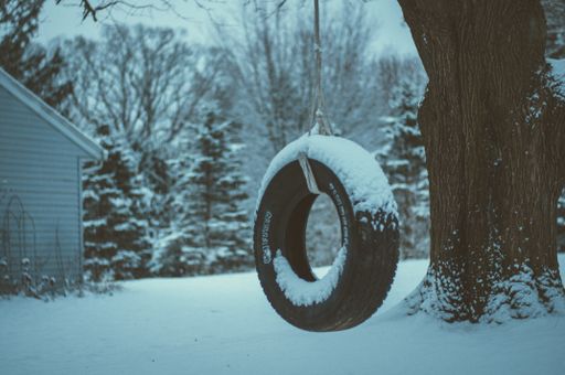 A shallow focus shot of a tire swing hanging on a tree covered with white snow during winter