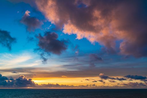 Vibrant sunset over the ocean with dramatic clouds and a colorful sky, creating a serene and picturesque seascape.