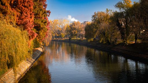 Scenic autumn landscape with vibrant foliage and a serene river reflecting the clear blue sky.