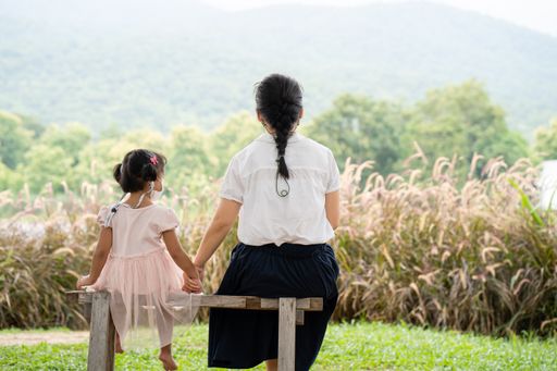 A rear view of a Southeast Asian mother and daughter sitting on a bench facing mountain scape