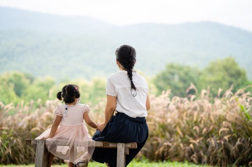 A mother with her little daughter sitting on the bench looking at the fields and mountains