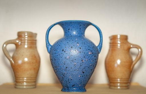 A blue ceramic vase with handles contrasts with two smaller brown jugs, showcasing handmade ceramics' beauty and varying styles.