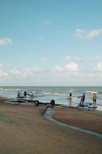 Fishermen pulling nets on a sandy beach under a clear blue sky, capturing the essence of coastal life.