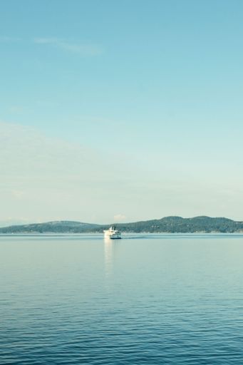 A serene view of a ferry sailing on calm waters with distant hills under a clear blue sky.