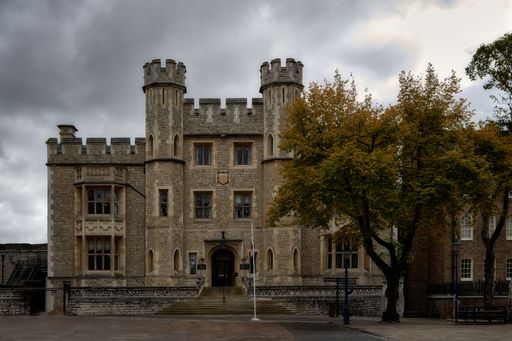 Historic castle with medieval architecture under a cloudy sky, featuring stone walls and turrets, surrounded by autumn trees.