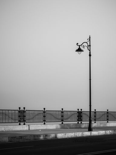 A vertical shot of a street light with a sidewalk and fence