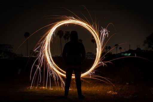 An eerie scenery of a silhouette of a man swirling shiny lights in circles on the beach at night