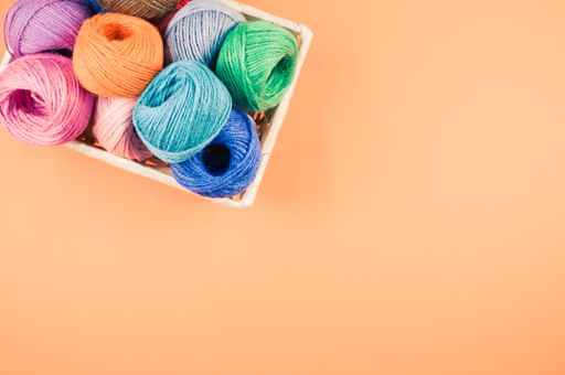 A basket full of colorful yarn rolls isolated on an orange background with free space for text