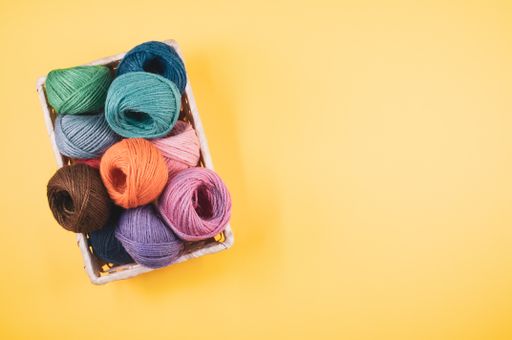 A basket full of colorful yarn rolls isolated on a yellow background with free space for text