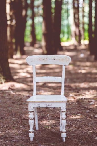 A vertical shot of an old white wooden chair in a forest during daylight